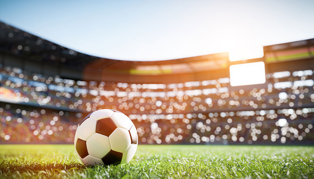 Soccer ball on pitch with stadium in background